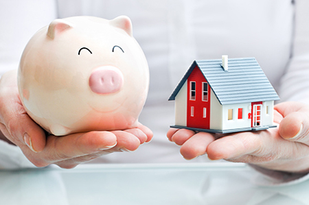 Hands holding a  piggy bank and a house model